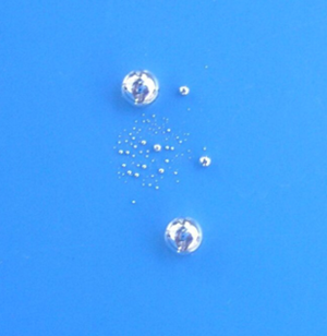 A close-up of mercury beading on a surface. The mercury forms shiny spherical drops.